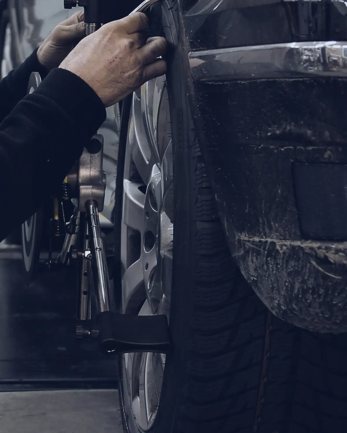 Hands on a tyre, with a wheel alignment clamp fitted to its alloy rim