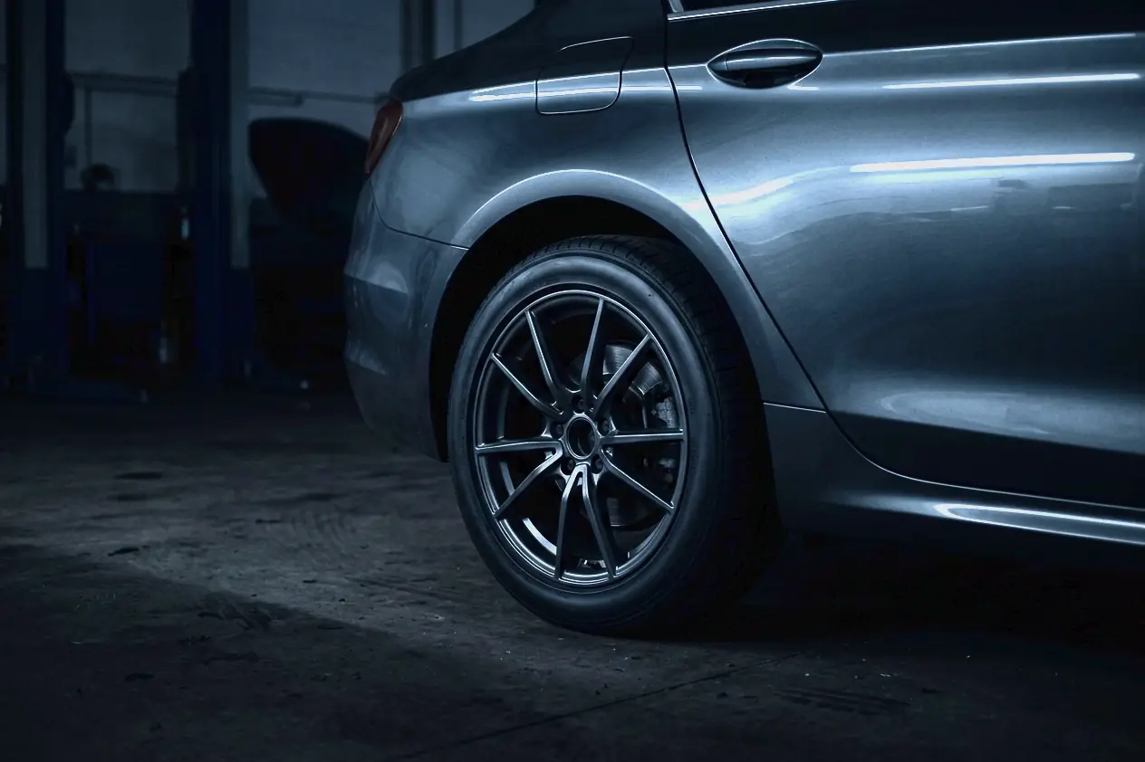 The dark grey flank and rear wheel of a modern car in a dim garage