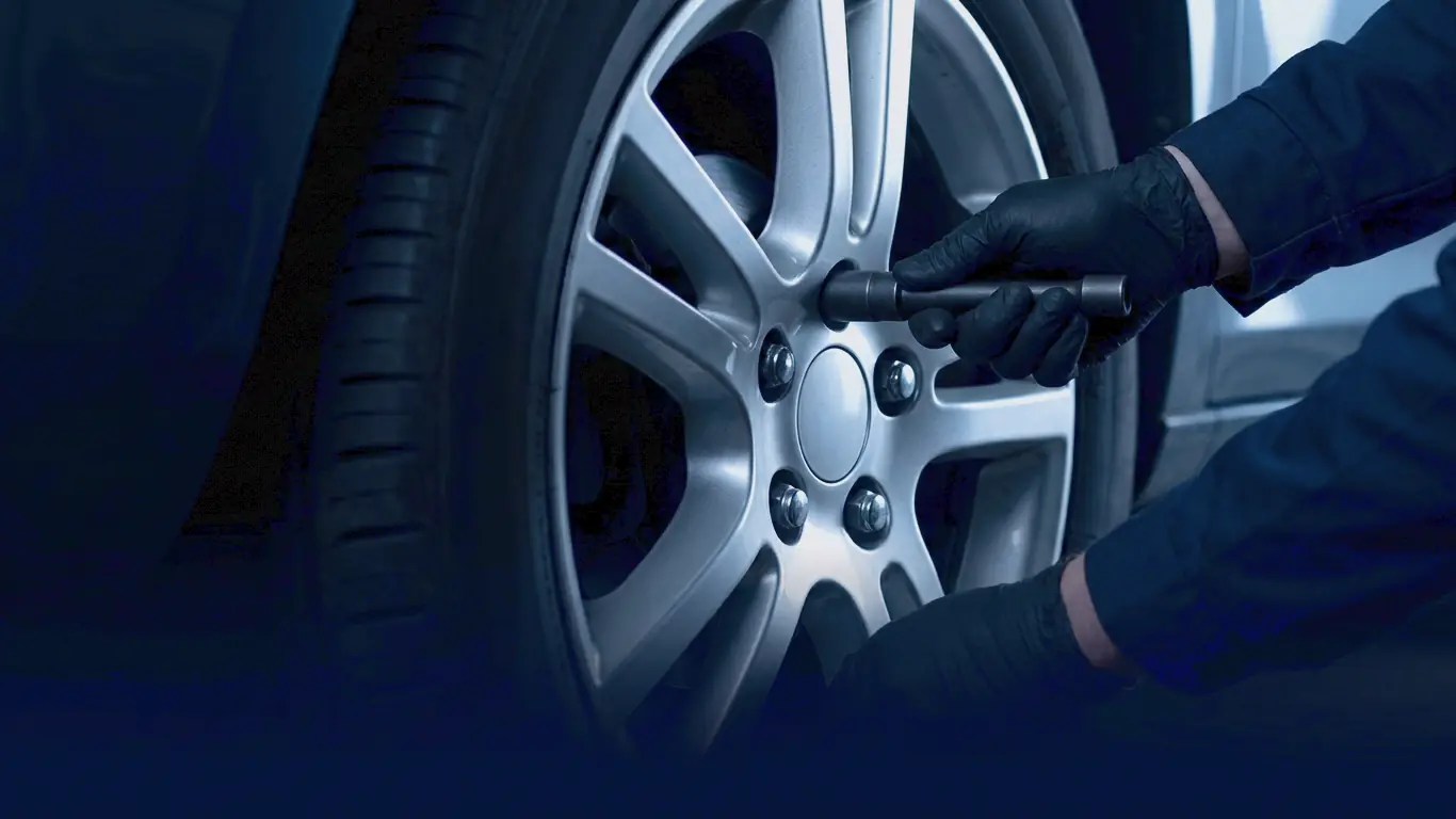 A gloved hand turning a wheel nut with a plain socket wrench on a silver alloy wheel
