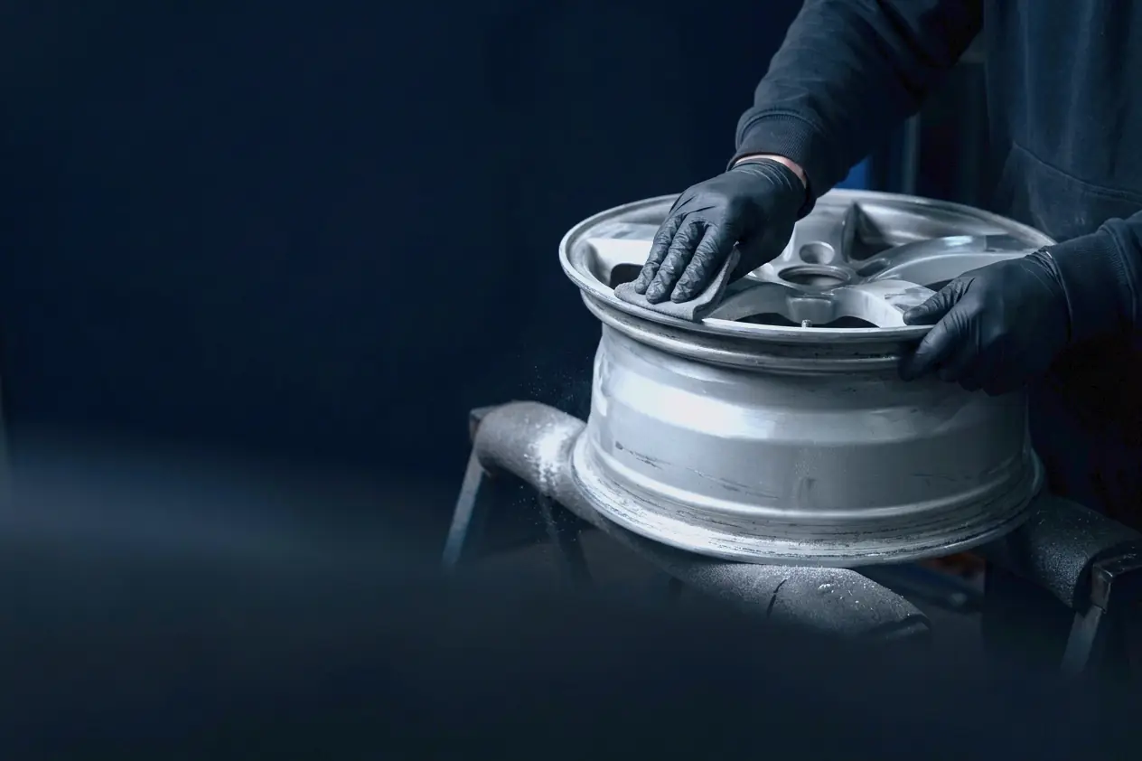 A gloved hand sanding the lip of a bare alloy rim on a padded stand