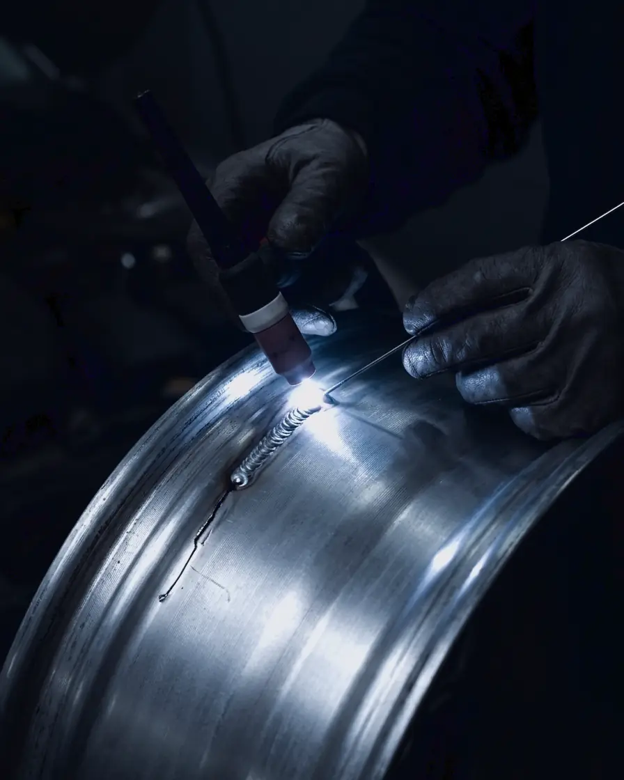 Close-up of a TIG torch laying a weld bead along a crack in an alloy rim