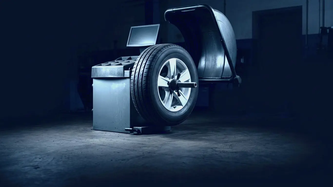A wheel mounted on a wheel-balancing machine, its hood raised, in a dark bay